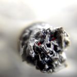 Hombre fumando solo en la oscuridad, con humo iluminado.