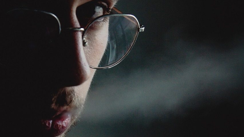 Hombre fumando solo en la oscuridad, con humo iluminado.