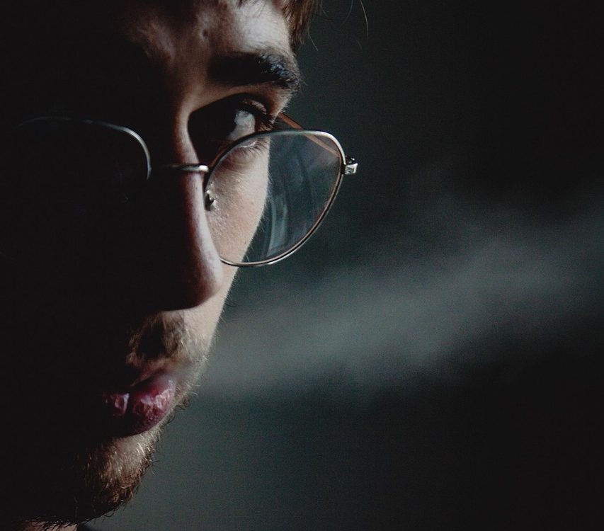Hombre fumando solo en la oscuridad, con humo iluminado.